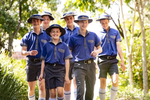 Six boys in blue and grey uniform walking along a tree-lined path